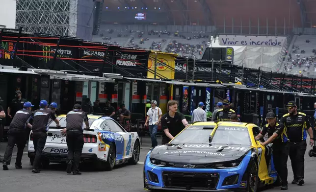 Mechanics of Justin Haley, right, and Noah Gragson push their cars on the paddock prior to a practice session for the NASCAR Cup Series auto race at the Hermanos Rodriguez race track in Mexico City, Friday, June 13, 2025. (AP Photo/Fernando Llano)