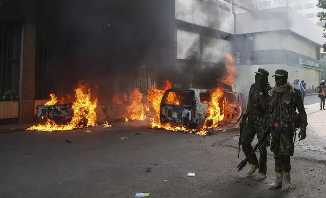 Riot police officers walk past cars set on fire during a protest over the death in police custody of blogger Albert Ojwang, in Nairoby, Kenya, Thursday, June 12, 2025. (AP Photo/Andrew Kasuku)