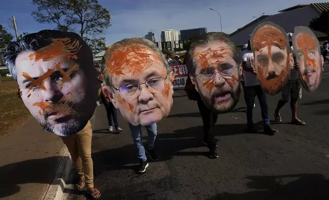 People carry cut-outs of the faces of senators to protest a bill before Congress that would change environmental licensing laws, on World Environment Day in Brasilia, Brazil, Thursday, June 5, 2025. (AP Photo/Eraldo Peres)