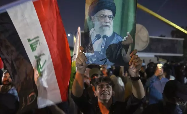A protest holds a portrait of Iran's Supreme Leader Ayatollah Ali Khamenei during a protest against Israeli attacks on multiple cities across Iran, at a bridge leading to the fortified Green Zone where the U.S. embassy is located in Baghdad, Iraq, Saturday, June 14, 2025. (AP Photo/Hadi Mizban)