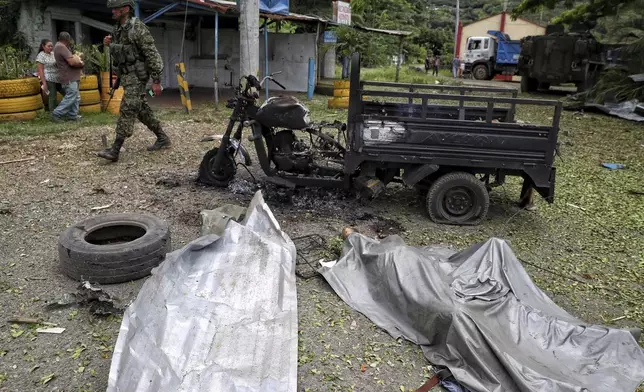 A soldier walks past the body of a man covered in plastic, right, and his charred motorcycle, after the person was killed by a bomb that exploded in Guachinte, Cauca Valley, Colombia, Tuesday, June 10, 2025. (AP Photo/Santiago Saldarriaga)