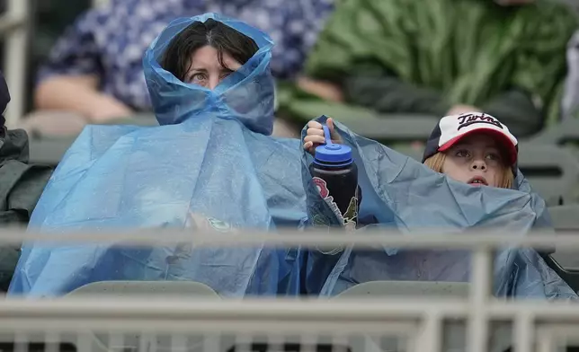 Fans are covered up with ponchos during a rain delay before a baseball game between the Minnesota Twins and Seattle Mariners, Thursday, June 26, 2025, in Minneapolis. (AP Photo/Abbie Parr)