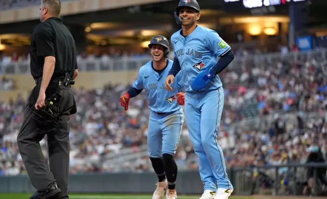 Toronto Blue Jays'Andrés Giménez (0), front, and Ernie Clement (22) celebrate after scoring during the fifth inning of a baseball game against the Minnesota Twins, Friday, June 6, 2025, in Minneapolis. (AP Photo/Abbie Parr)