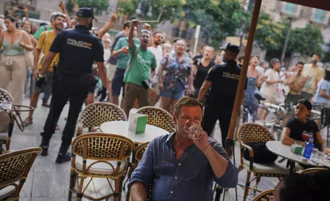 Tourists sit in a restaurant as people protest against overtourism in the Balearic island of Mallorca, Spain, Sunday, June 15, 2025. (AP Photo/Joan Mateu Parra)