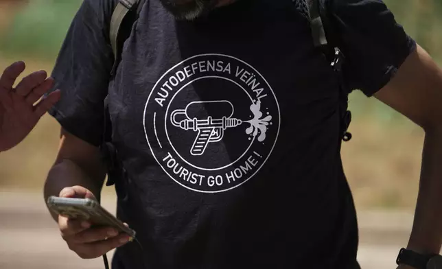A person wears a t shirt with the message reading 'Neighborhood auto defense - Tourists go home' during a protest against overtourism in Barcelona, Spain, Sunday, June 15, 2025. (AP Photo/Pau Venteo)