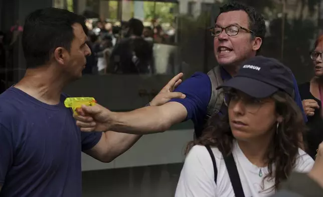 A plain clothed police officer, left, tries to stop a man shooting a water pistol during a protest against overtourism in Barcelona, Spain, Sunday, June 15, 2025. (AP Photo/Pau Venteo)