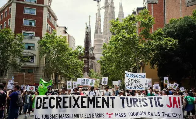 People march near the Sagrada Familia basilica during a protest against overtourism in Barcelona, Spain, Sunday, June 15, 2025. Main banners read 'Decrease level of tourism now', Mass tourism kills neighborhoods' and 'Tarragona without cruise ships' (AP Photo/Pau Venteo)