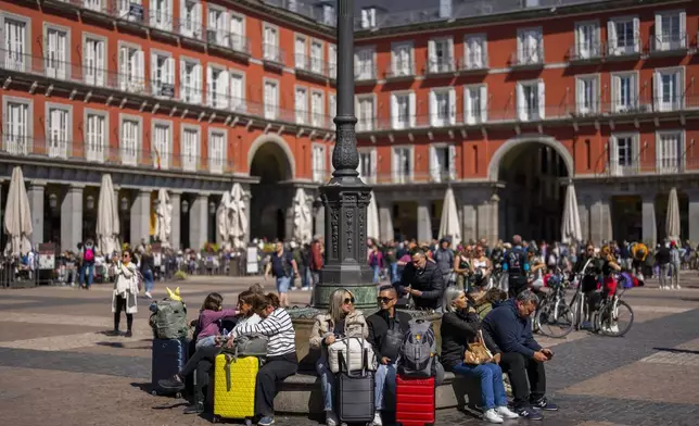 FILE - Tourists sit on a public bench at Plaza Mayor in downtown Madrid, Spain, April 29, 2024. (AP Photo/Bernat Armangue, File)