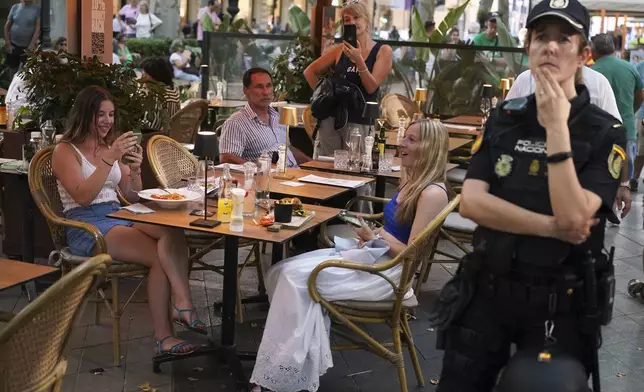 A police officer stands next to bar as people march during a protest against overtourism in the Balearic island of Mallorca, Spain, Sunday, June 15, 2025. (AP Photo/Joan Mateu Parra)