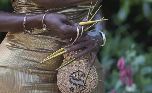A racegoer in a gold dress with long gold nails and a dollar symbol handbag poses for a photograph on the third day of the Royal Ascot horse race meeting, traditionally called Ladies Day, at Ascot, England, Thursday, June 19, 2025. (AP Photo/Kin Cheung)