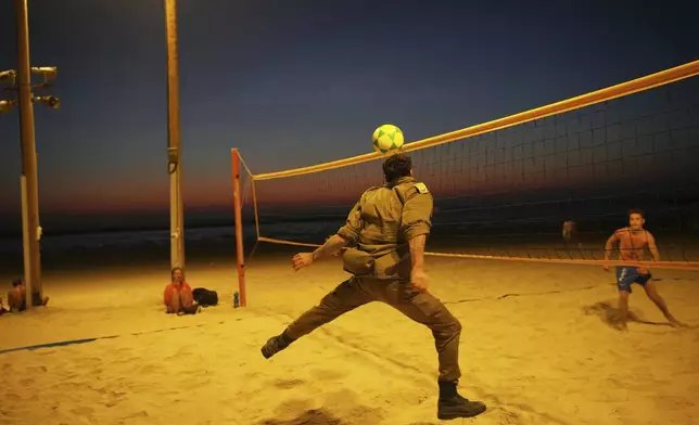An Israeli soldier plays beach volley at sunset in Tel Aviv's beachfront Thursday, June 19, 2025. (AP Photo/Ohad Zwigenberg)