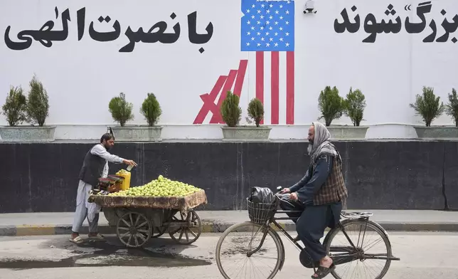 A cyclist passes in front of the former US embassy while a vendor waits for customers, in Kabul, Afghanistan, Thursday, June 5, 2025. (AP Photo/Ebrahim Noroozi)