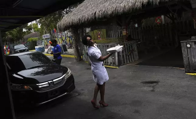 Yvette Chatelain, a sales rep for Haitian food products, strikes a pose as she leaves with her meal, at Chef Creole restaurant in Miami's Little Haiti neighborhood, Thursday, June 5, 2025. (AP Photo/Rebecca Blackwell)