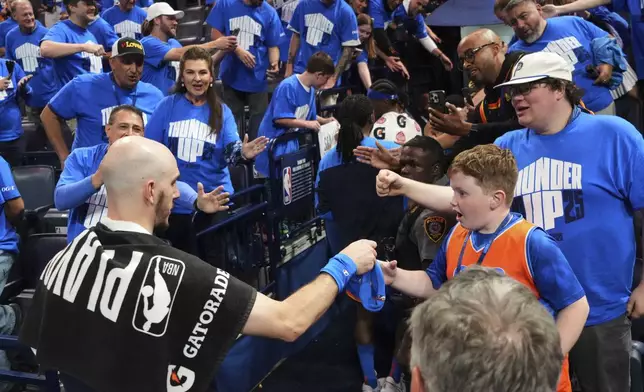 Oklahoma City Thunder's Alex Caruso, bottom left, hands a souvenir to a young fan after the team's win against the Denver Nuggets in Game 7 in the Western Conference semifinals of the NBA basketball playoffs, Sunday, May 18, 2025, in Oklahoma City. (AP Photo/Kyle Phillips)