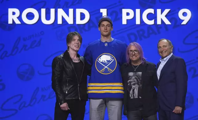Radim Mrtka, middle left, stands between The Goo Goo Dolls' John Rzeznik, left, and Robby Takac, middle right, and NHL commissioner Gary Bettman after being drafted by the Buffalo Sabres during the NHL hockey draft Friday, June 27, 2025, in Los Angeles. (AP Photo/Damian Dovarganes)