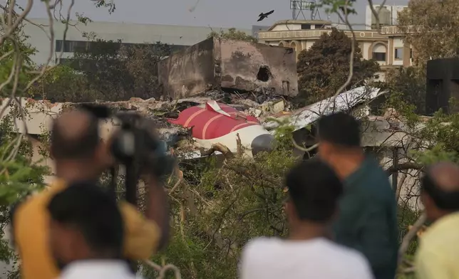 Onlookers watch wreckage from Thursday's Air India plane crash lying atop a building in Ahmedabad, India, Saturday, June 14, 2025. (AP Photo/Rafiq Maqbool)