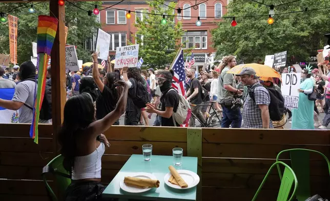 A person sitting in a restaurant records demonstrators as they march during a protest taking place on the day of a military parade commemorating the Army's 250th anniversary, coinciding with President Donald Trump's 79th birthday, Saturday, June 14, 2025, in Washington. (AP Photo/Alex Brandon)