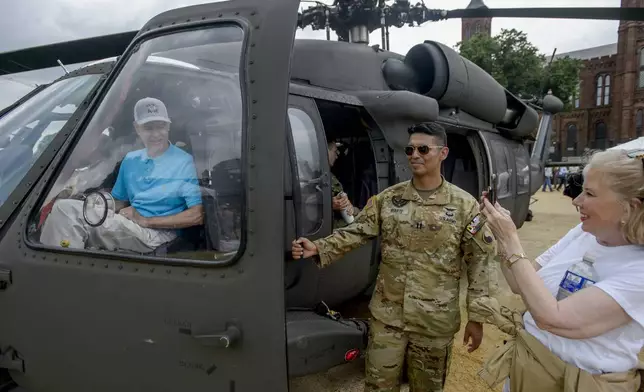 Dale Booth, left, of Tyler, Texas, poses in a Blackhawk helicopter for his wife Jan Booth, right, during the festival event to honor the Army's 250th anniversary, coinciding with President Donald Trump's 79th birthday, Saturday, June 14, 2025, on the National Mall in Washington. (AP Photo/Rod Lamkey, Jr.)