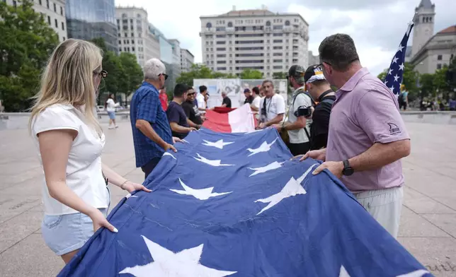 People fold a large American flag at Freedom Plaza before a parade commemorating the Army's 250th anniversary, coinciding with President Donald Trump's 79th birthday, Saturday, June 14, 2025, in Washington. (AP Photo/Manuel Balce Ceneta)
