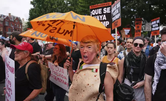 A demonstrator wearing a President Donald Trump mask marches with others during a protest taking place on the day of a military parade commemorating the Army's 250th anniversary, coinciding with President Donald Trump's 79th birthday, Saturday, June 14, 2025, in Washington. (AP Photo/Evan Vucci)