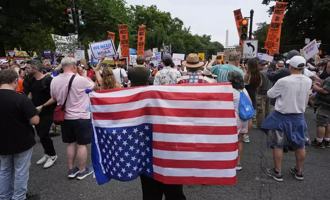 A demonstrator carries an American flag upside-down near the White House during a protest taking place on the day of a military parade commemorating the Army's 250th anniversary, coinciding with President Donald Trump's 79th birthday, Saturday, June 14, 2025, in Washington. (AP Photo/Alex Brandon)
