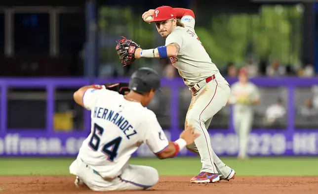 Philadelphia Phillies second base Bryson Stott, right, turns a double play as Miami Marlins' Heriberto Hernandez (64) slides during the second inning of a baseball game, Thursday, June 19, 2025, in Miami. (AP Photo/Michael Laughlin)