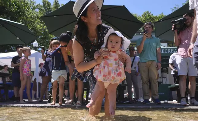 With temperatures hovering near 100 degrees, Boston Mayor Michelle Wu dips her daughter Mira's toes into the Frog Pond, on Boston Common, Tuesday, June 24, 2025, in Boston. (AP Photo/Charles Krupa)