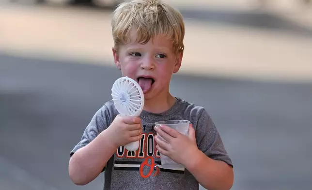 Asher Gillen, 3, uses a battery-powered fan while holding a cup of ice to cool off during hot weather before a baseball game between the Baltimore Orioles and the Texas Rangers, Monday, June 23, 2025, in Baltimore. (AP Photo/Stephanie Scarbrough)