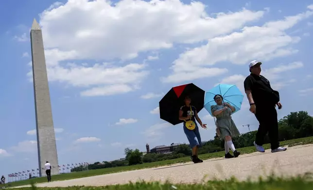 People use umbrellas to shield themselves from the sun as they walk along the National Mall, Tuesday, June 24, 2025, in Washington, past the Washington Monument. (AP Photo/Julia Demaree Nikhinson)