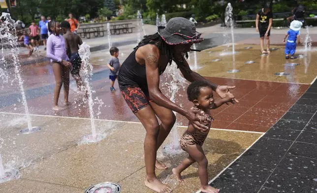 Shanae Brooks cools off with her daughter, Devynn, 2, at a splash pad Friday, June 20, 2025, in Cincinnati. (AP Photo/Joshua A. Bickel)