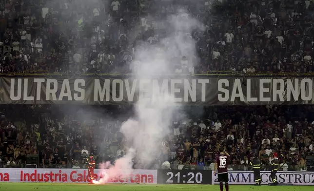 A firefighter tends to a flare thrown onto the pitch during a playoff between Sampdoria and Salernitana to stay in Serie B, which caused the suspension of the match, at the at the Arechi Stadium in Salerno, southern Italy, Sunday, July 22, 2025. (Alessandro Garofalo/LaPresse via AP)