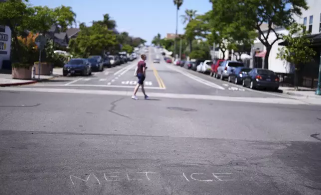 A man crosses a street where graffiti reads "melt ICE," at the site of a recent ICE operation at a popular Italian restaurant in the neighborhood of South Park Monday, June 2, 2025, in San Diego. (AP Photo/Gregory Bull)