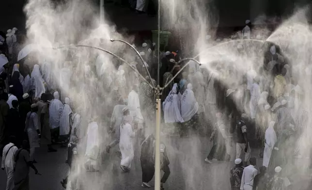 Cooling fans spray water over Muslim pilgrims as they walk to cast stones at pillars in the symbolic stoning of the devil, the last rite of the annual Hajj, in Mina near the holy city of Mecca, Saudi Arabia, Saturday, June 7, 2025. (AP Photo/Amr Nabil)