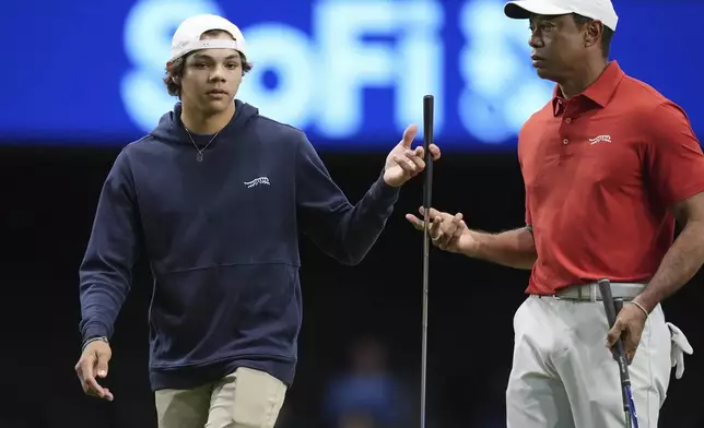 FILE - Charlie Woods, left, hands a club to his father Tiger Woods during warm-ups for a match as part of part of the TMRW Golf League, in Palm Beach Gardens, Fla., Jan. 27, 2025. (AP Photo/Rebecca Blackwell, File)