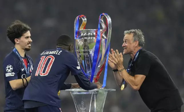 PSG's head coach Luis Enrique and players Vitinha, left, and Ousmane Dembele look at the trophy at the end of the Champions League final soccer match between Paris Saint-Germain and Inter Milan at the Allianz Arena in Munich, Germany, Saturday, May 31, 2025. (AP Photo/Luca Bruno)