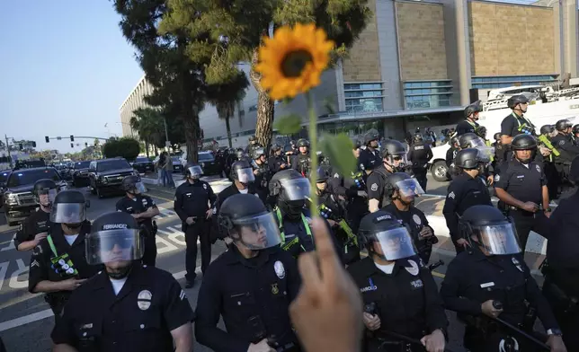 A protester offers a flower to Los Angeles police officers in riot gear while they attempt to clear a street in downtown Los Angeles on Monday, June 9, 2025. (AP Photo Jae Hong)