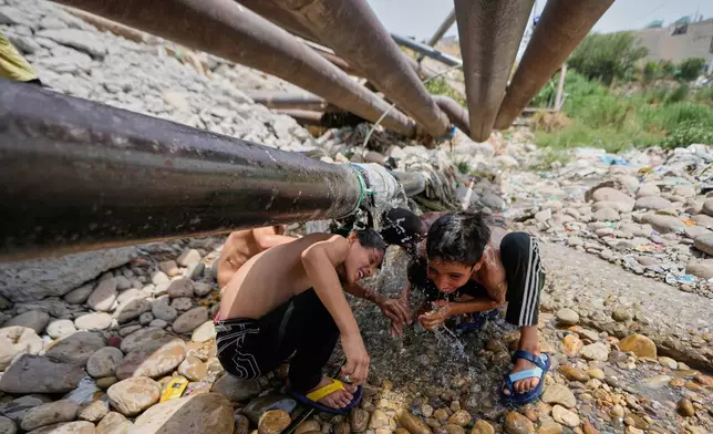 Boys cool off with water leaking from a pipeline on a hot summer day in Jammu, India, Tuesday, June 10, 2025. (AP Photo/Channi Anand)