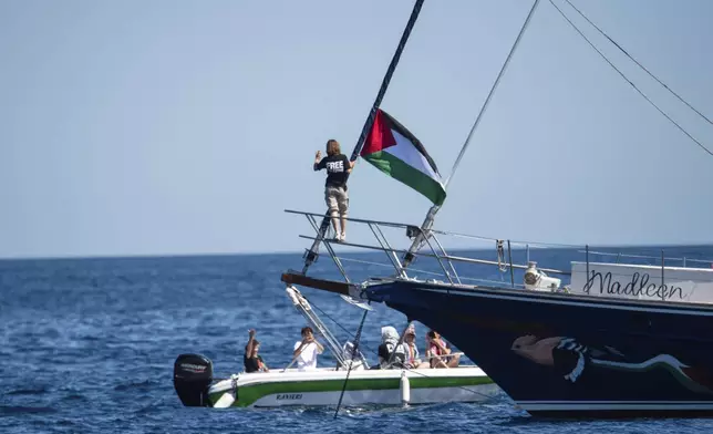 Climate activist Greta Thunberg stands near a Palestinian flag after boarding the Madleen boat and before setting sail for Gaza along with activists of the Freedom Flotilla Coalition, departing from the Sicilian port of Catania, Italy, Sunday, June 1, 2025. (AP Photo/Salvatore Cavalli)