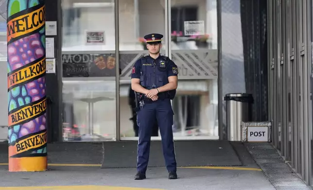 A police officer guards the entrance of a school where a former student opened fire the day before fatally wounding 10 people and injuring many others before taking his own life, Graz, Austria, Wednesday, June 11, 2025. (AP Photo/Darko Bandic)