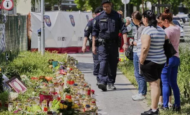 People and police officers gather near candles and flowers outside a school where a former student opened fire two days before, in Graz, Austria, Thursday, June 12, 2025. (AP Photo/Darko Bandic)