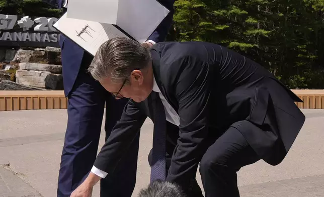 Britain's Prime Minister Keir Starmer picks up papers that President Donald Trump dropped as they meet on the sidelines of the G7 Summit, Monday, June 16, 2025, in Kananaskis, Canada. (AP Photo/Mark Schiefelbein)