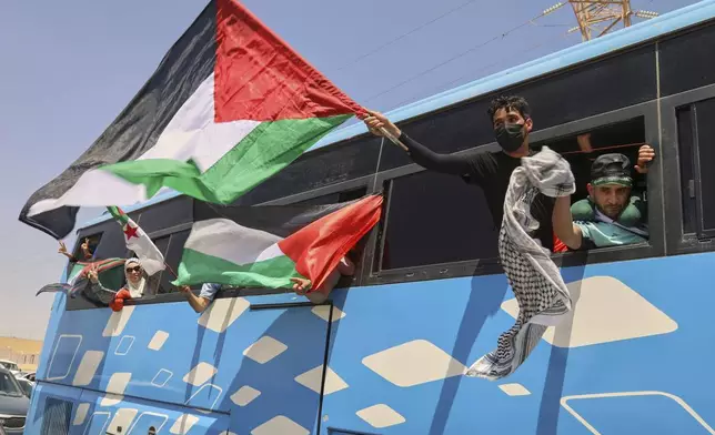 Members of a humanitarian convoy of at least 1,500 people, including activists and supporters from Algeria and Tunisia, wave Palestinian flags from a bus as the group travels toward Gaza via Egypt's Rafah Crossing, in Zawiya, Libya, Tuesday, June 10, 2025. (AP Photo/Yousef Murad)