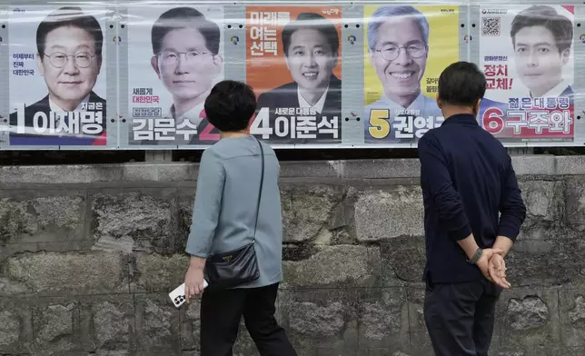 People watch posters showing candidates for the June 3 presidential election in Seoul, South Korea, Monday, June 2, 2025. (AP Photo/Ahn Young-joon)