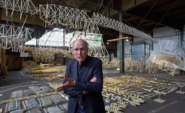 Dutch artist Theo Jansen is interviewed in front of his 'strandbeesten' or Beach Beasts, wind-powered creatures made from yellow plastic tubes, displayed during an exhibit in Delft, Netherlands, Thursday, June 5, 2025. (AP Photo/Peter Dejong)