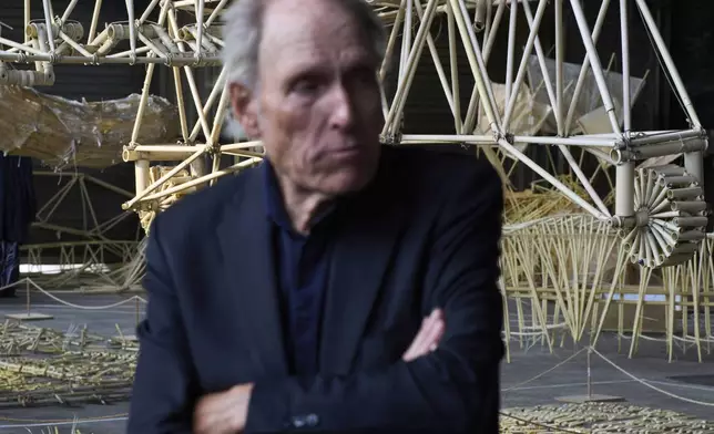 Dutch artist Theo Jansen is interviewed in front of his 'strandbeesten' or Beach Beasts, wind-powered creatures made from yellow plastic tubes, displayed during an exhibit in Delft, Netherlands, Thursday, June 5, 2025. (AP Photo/Peter Dejong)