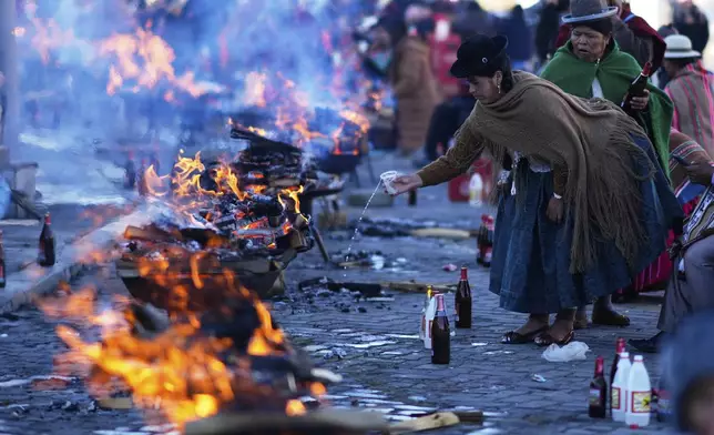 A woman sprinkles liquor on a bonfire of offerings during a celebration of the Andean New Year 5533 marking the Southern Hemisphere's winter solstice, in El Alto, Bolivia, Saturday, June 21, 2025. (AP Photo/Juan Karita)