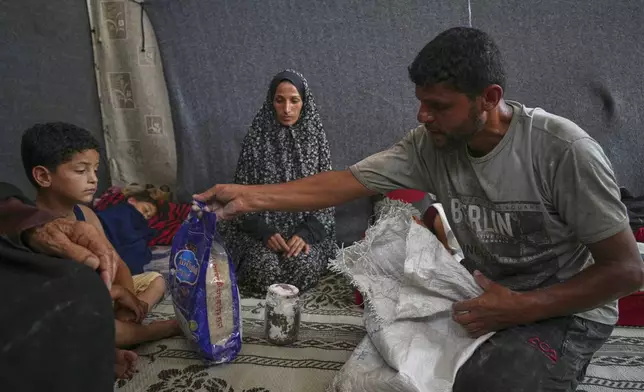 Omar al-Hobi, 43, from Rafah, unpacks a bag of food he collected at a distribution center run by private contractor the Gaza Humanitarian Foundation in the southern Gaza Strip, as he arrives at his family's tent in Khan Younis, Tuesday, June 10, 2025. At left are his children and his wife, Anwaar Saleh.(AP Photo/Abdel Kareem Hana)