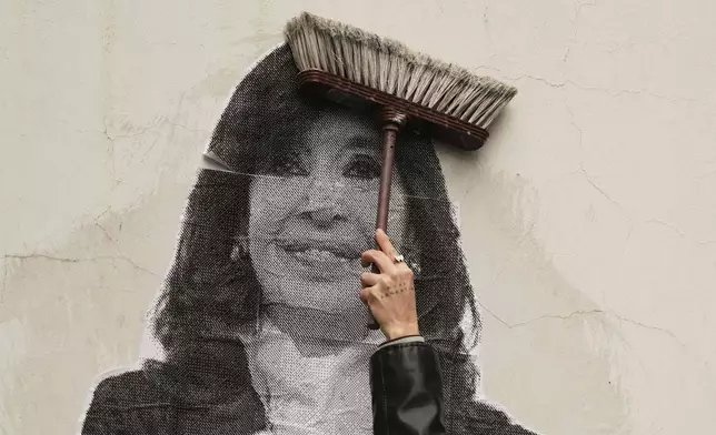 A supporter of Argentina's former President Cristina Fernandez uses a boom to paste a photo of her on the wall outside her home after the nation's Supreme Court upheld Fernandez's corruption conviction in Buenos Aires, Argentina, Tuesday, June 17, 2025. (AP Photo/Natacha Pisarenko)