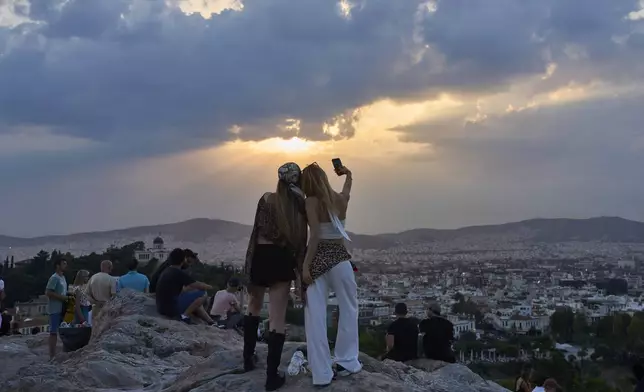 Women take a selfie on Aeropagous hill in Athens as the sun sets, Friday, June 20, 2025. (AP Photo/Petros Giannakouris)