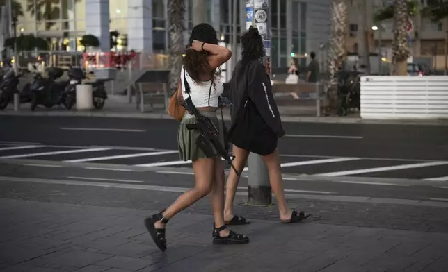 An off duty Israeli soldier carries an M16 assault rifle as she walks near Tel Aviv's beachfront Thursday, June 19, 2025. (AP Photo/Ohad Zwigenberg)